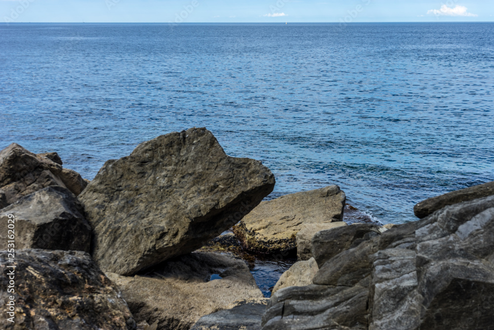 Italy,Cinque Terre,Riomaggiore, a person sitting on a rock near the ocean