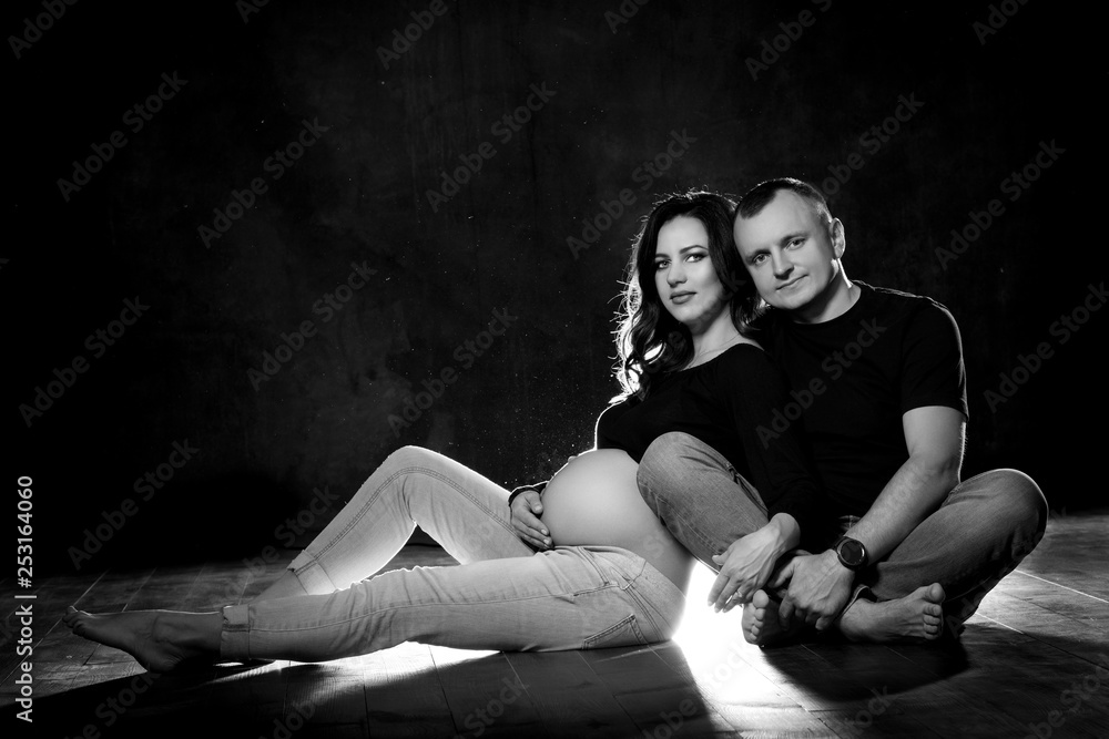 Handsome pregnant couple woman and man an posing on dark black background. Family love and expectation of the baby Handsome pregnant couple woman and man an posing on dark black background. Family love and expectation of the baby