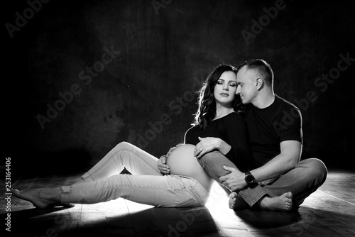 Handsome pregnant couple woman and man an posing on dark black background. Family love and expectation of the baby