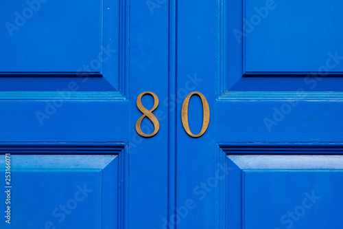 House number 80 in bronze numerals on a blue painted wooden door