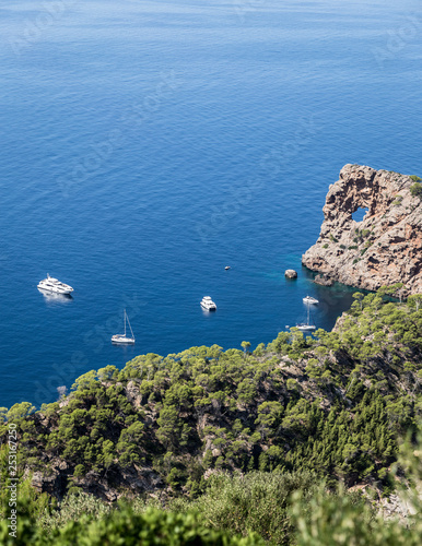 a rock with a hole at the top; a small sea bay near the rocks; white yachts near the shore; view from above to shore cliffs and sea
