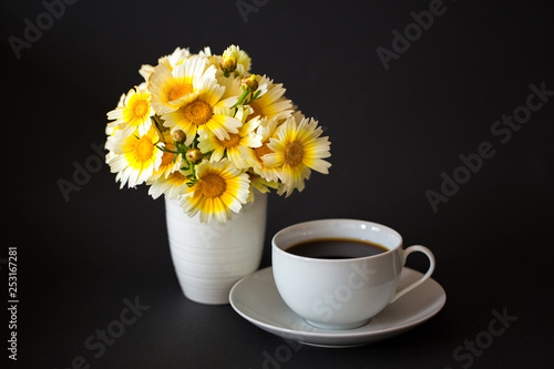Bouquet of daisies in a vase and a cup of hot coffee / tea on a black background. Horizontal. Space for text