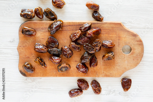 Dried dates on rustic wooden board over white wooden surface, top view. From above, overhead, flat lay. Close-up.