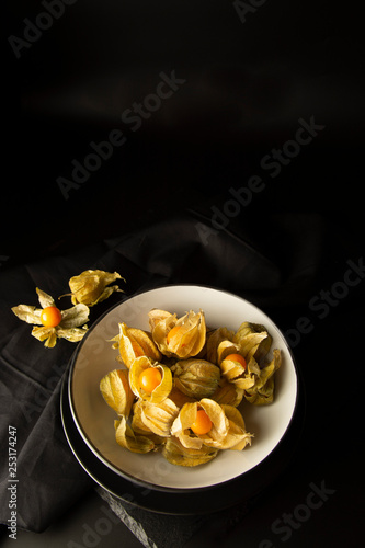 Physalis flowers  fruits isolatedin black plate  on a black background. Orange berry fruits  decorations for cakes.