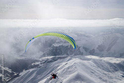 Paragliding at snowy mountains over ski resort at sunny winter day. Caucasus Mountains. Georgia, region Gudauri.