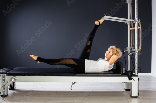 Pilates. Woman in black and white clothes practicing stretching exercise on reformer in gym
