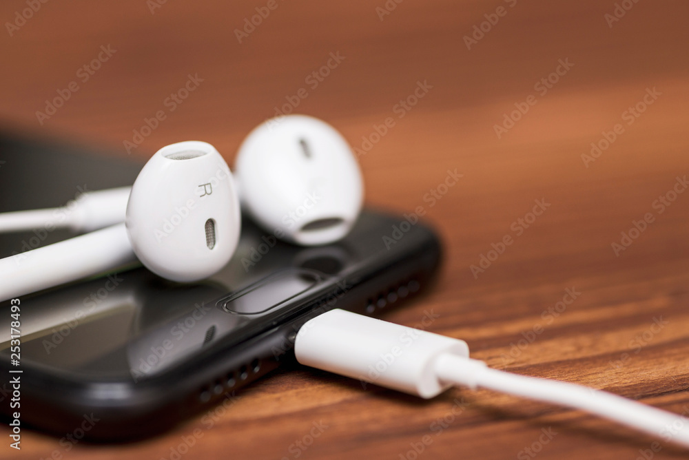 Smartphone with earphone on wooden background. White earphones and mobile phone on wooden background Smartphone with earphone on wooden background. White earphones and mobile phone on wooden background