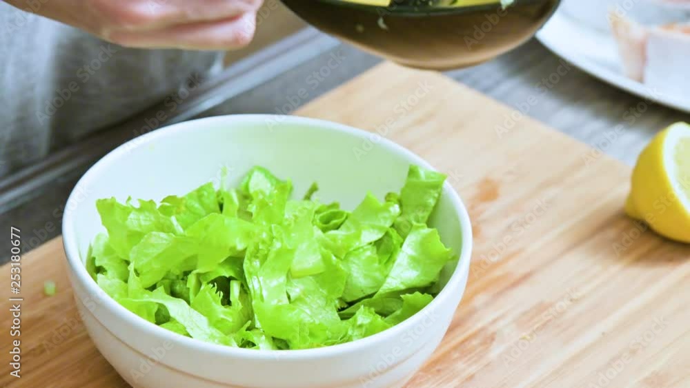 Close-up of female hands in a home kitchen are added to a vegetarian leaf salad sauce and mixed with a spoon on a wooden cutting board Close-up of female hands in a home kitchen are added to a vegetarian leaf salad sauce and mixed with a spoon on a wooden cutting board