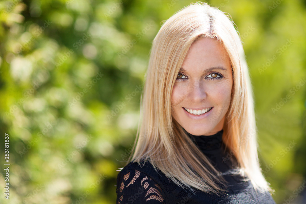 Closeup of a pretty blond smiling at the camera. She is outside on a trees background Closeup of a pretty blond smiling at the camera. She is outside on a trees background