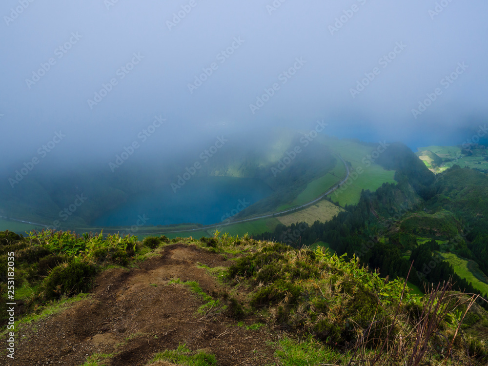 Stunning view on volcanic lakes. Green Lagoa de Santiago and blue Lagoa Azul with Sete Cidades village, partially covered by fog mist and clouds. Sao Miguel in the Azores, Portugal