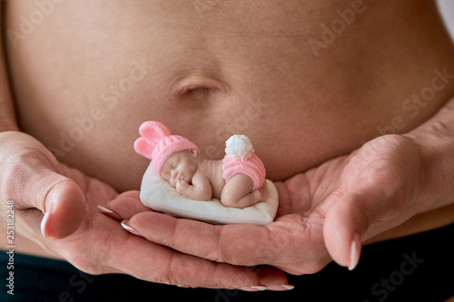 Pregnant young woomen holds a figurine of soap in the shape of a newborn baby girl in front of her belly on her palms on a white background. Close-up. photo