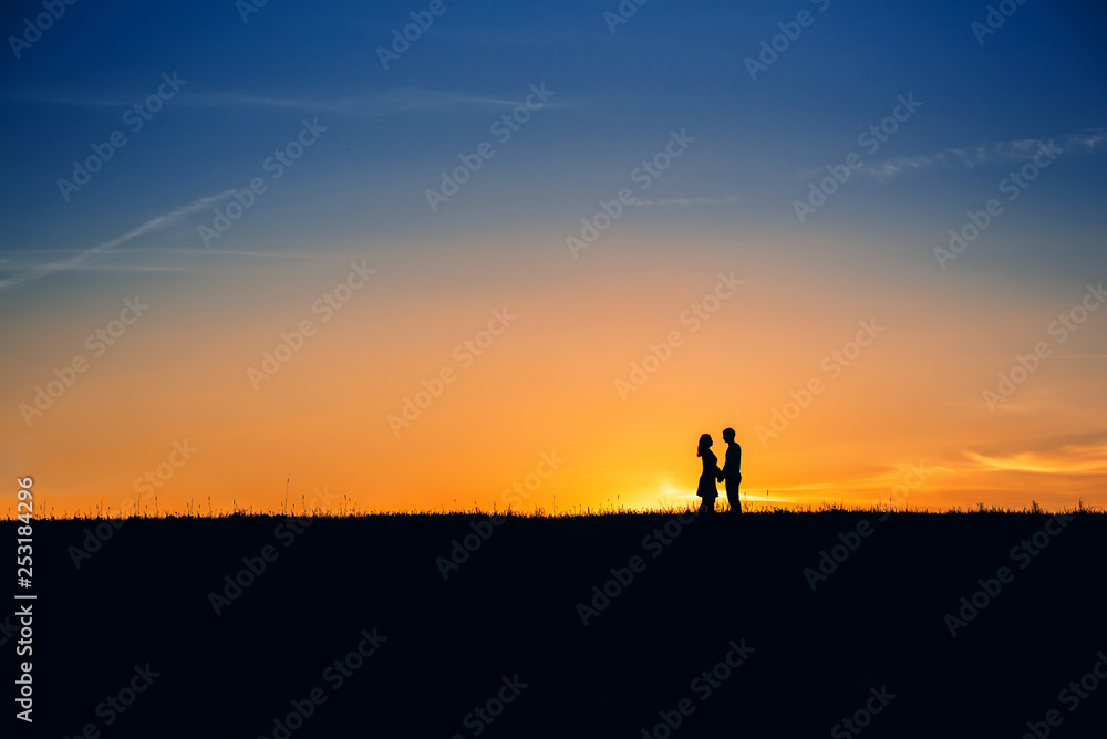silhouette of a couple in love on background of an orange sunset in summer