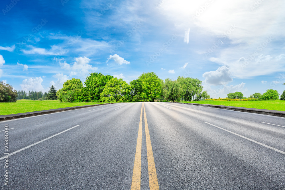 Straight asphalt road and green forest under blue sky Straight asphalt road and green forest under blue sky