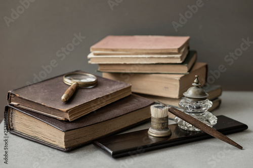 Several of antic books, set of old stationery, wooden pen, inkwell, magnifier close-up, vintage background. Concept of reading and education, memory and nostalgy