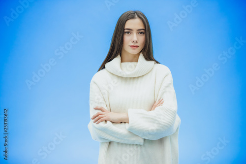 Girl in a white sweater on a blue background. Put your hand on your arm. The concept of hope for the opening of a new work