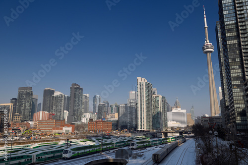Commuter GO trains and VIA train on tracks to Union Station Toronto with CN Tower and cityscape skyline of highrise buildings