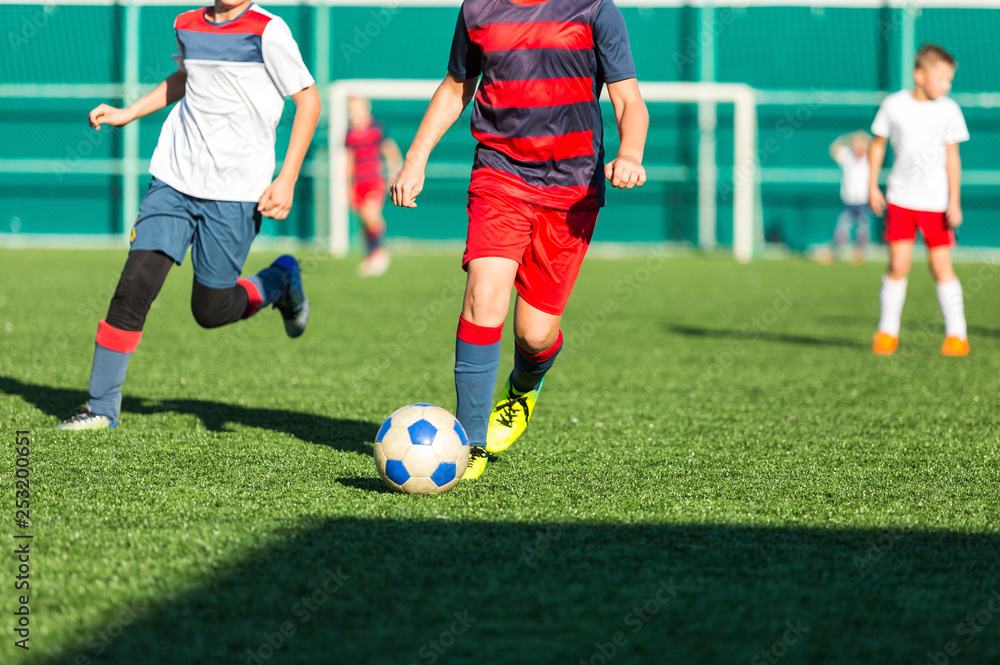 Boys in red white sportswear running on soccer field. Young footballers dribble and kick football ball in game. Training, active lifestyle, sport, children activity concept 