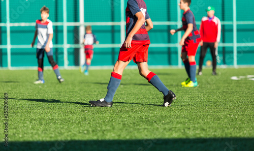 Boys in red white sportswear running on soccer field. Young footballers dribble and kick football ball in game. Training, active lifestyle, sport, children activity concept 