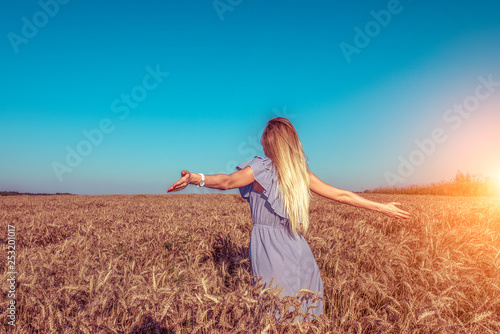 A girl in a dress, standing in wheat field in the summer, arms outstretched to the side, the farm and spikelets of wheat rest on nature.