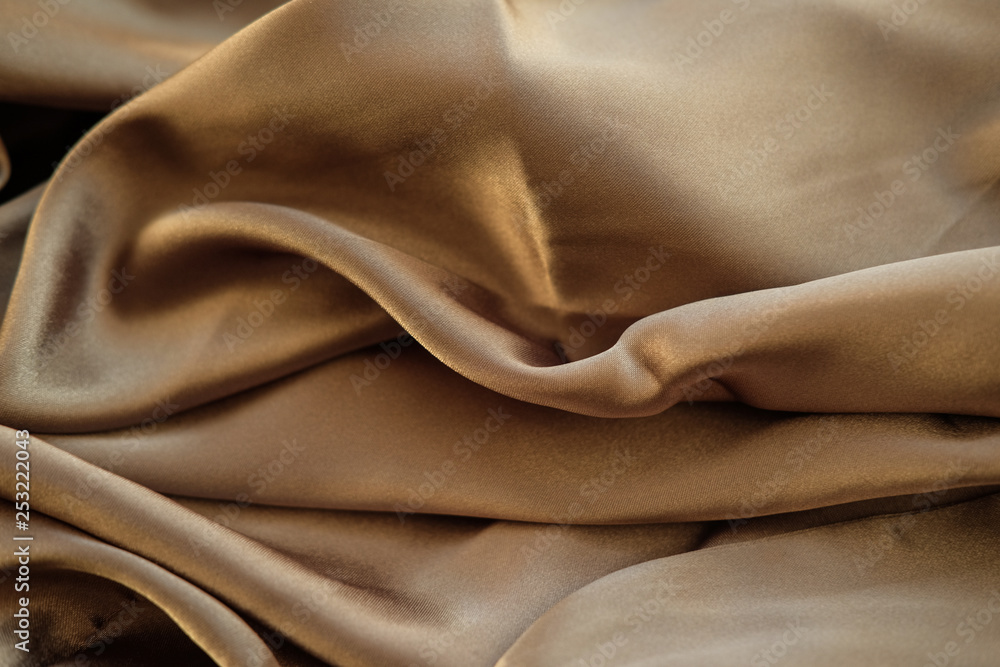The gold fabric is laid out waves. Satin fabric. Brown material textile. The gold fabric is laid out waves. Satin fabric. Brown material textile.