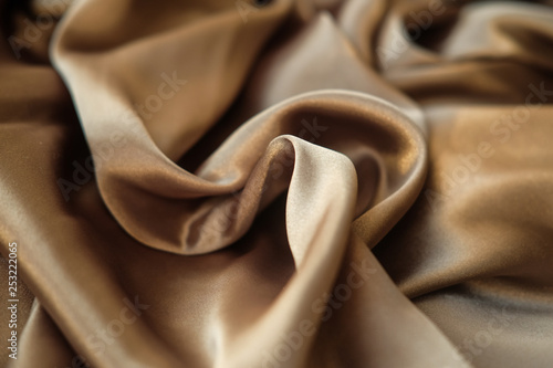 The gold fabric is laid out waves. Satin fabric. Brown material textile.