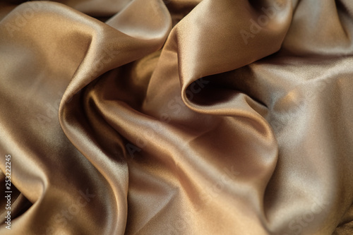 The gold fabric is laid out waves. Satin fabric. Brown material textile.