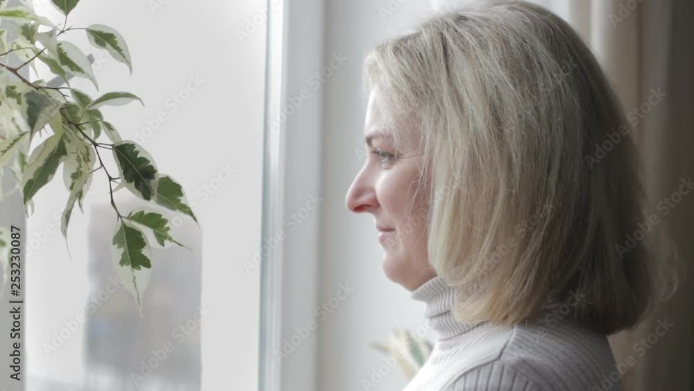 Adult woman looks out the window and turns her face to the camera Adult woman looks out the window and turns her face to the camera