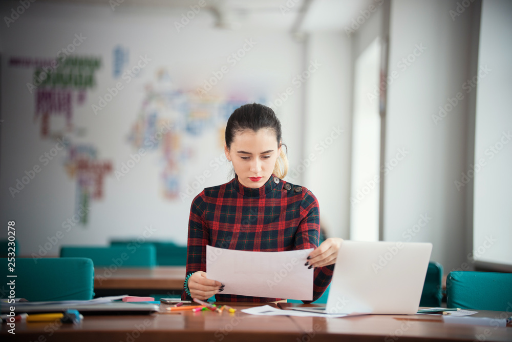 Young businesswoman working at office sitting by the table. Looking at papers Young businesswoman working at office sitting by the table. Looking at papers