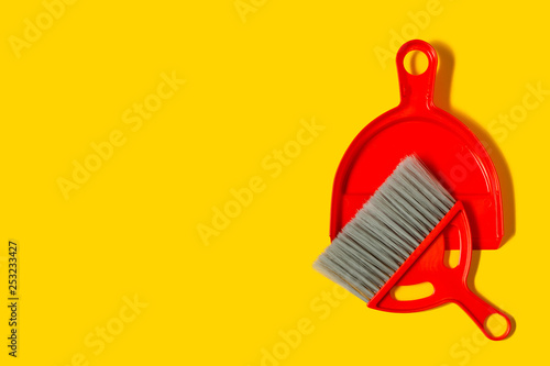 Red dustpan and brush lying on yellow background. In the style of pop art. Top view.