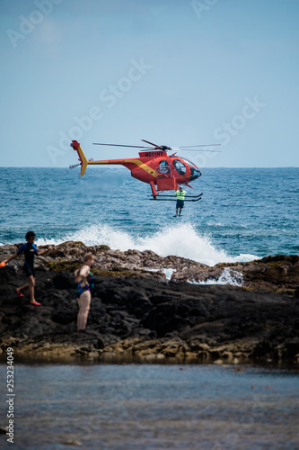 Helicopter dropping rescue diver off Hawaiian beach.