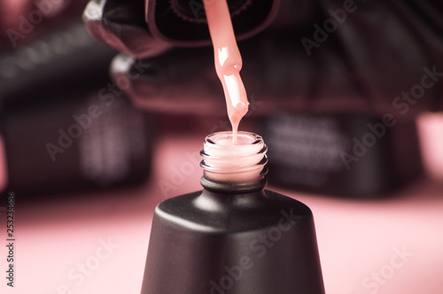 Nail salon: the master's hand in a black glove is dipping a brush with a drop in nail polish.