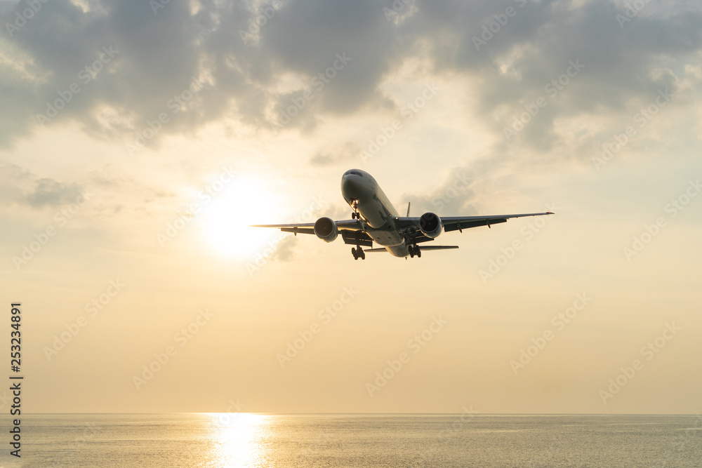 The plane sits above the sea at sunset.