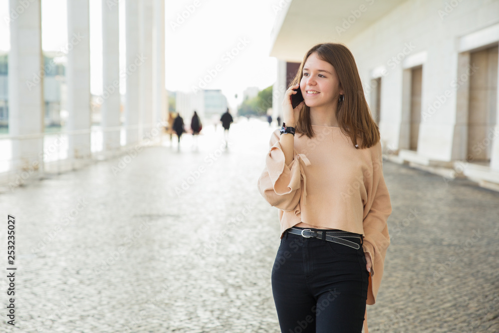 Fototapeta premium Happy female teenager talking on mobile phone outdoors