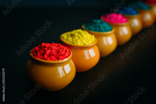 Line of colorful Holi powder in cups closeup. Bright colours for Indian holi festival in clay pots. Selective focus. Black background. Happy Holi greeting card