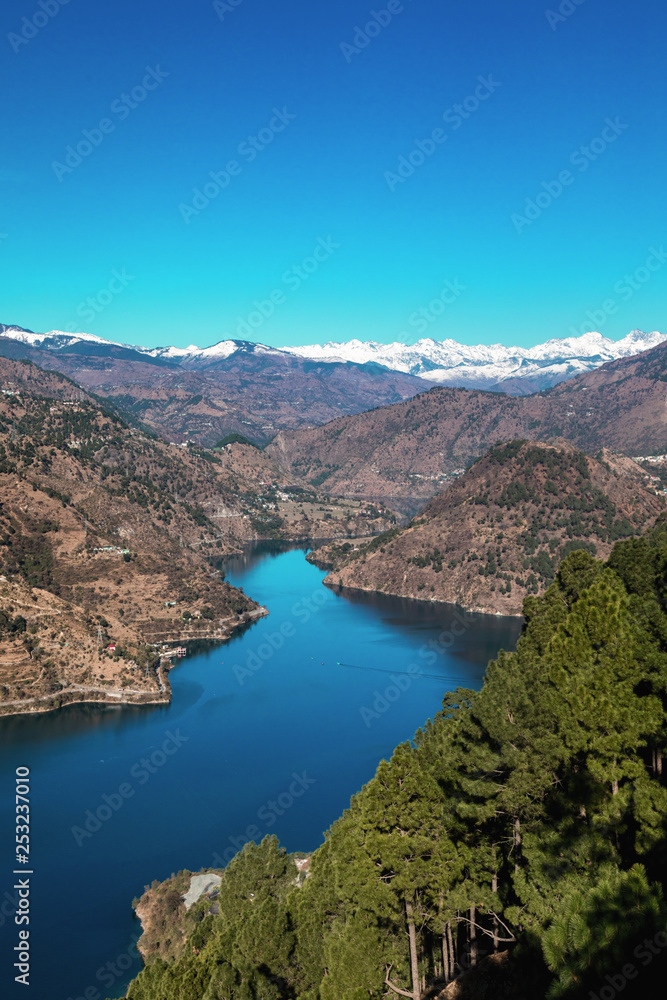 The snake shaped Chamera lake as seen from a top view point with snow covered peaks in the background