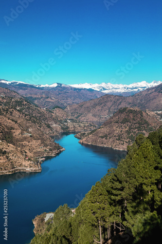 The snake shaped Chamera lake as seen from a top view point with snow covered peaks in the background