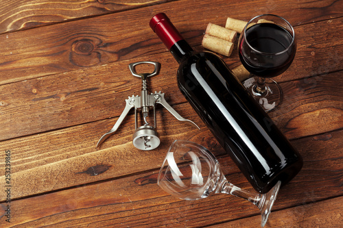 Red wine bottle, wine glass and corkscrew on wooden table background