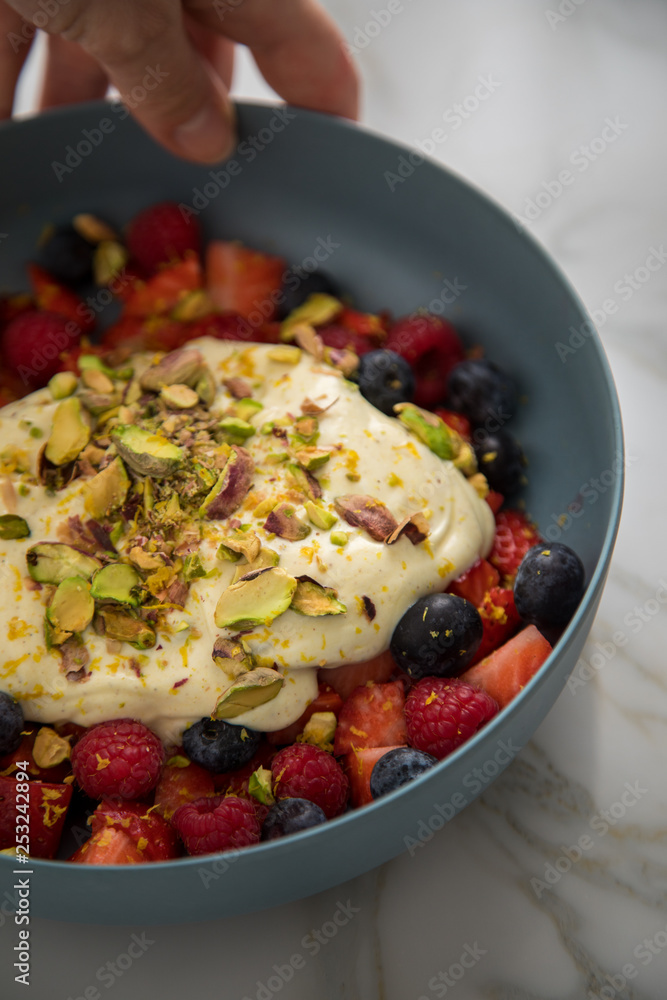 Frau isst Beeren Obstsalat mit Erdbeeren, Himbeeren, Blaubeeren, Pistazien, Zitronen Zesten, Leinöl Kurkuma Quark Creme in blauer Schale als Frühstück auf Marmor Hintergrund Frau isst Beeren Obstsalat mit Erdbeeren, Himbeeren, Blaubeeren, Pistazien, Zitronen Zesten, Leinöl Kurkuma Quark Creme in blauer Schale als Frühstück auf Marmor Hintergrund