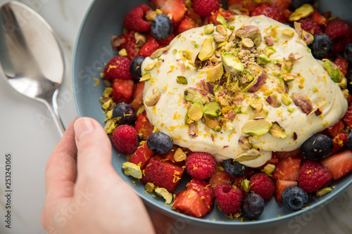 Wallpaper Mural Frau isst Beeren Obstsalat mit Erdbeeren, Himbeeren, Blaubeeren, Pistazien, Zitronen Zesten, Leinöl Kurkuma Quark Creme in blauer Schale als Frühstück auf Marmor Hintergrund Torontodigital.ca