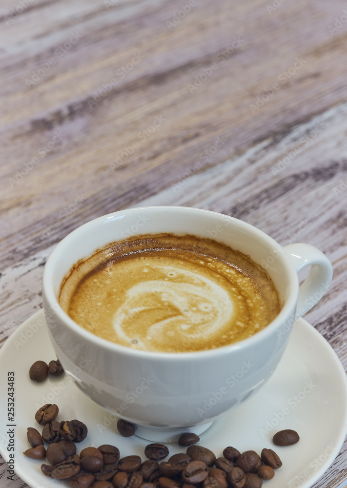 white cup with black coffee with milk. Handful of coffee beans on a wooden table. vertical view of drink with coffee. Copy space close up. white cup with black coffee with milk. Handful of coffee beans on a wooden table. vertical view of drink with coffee. Copy space close up.