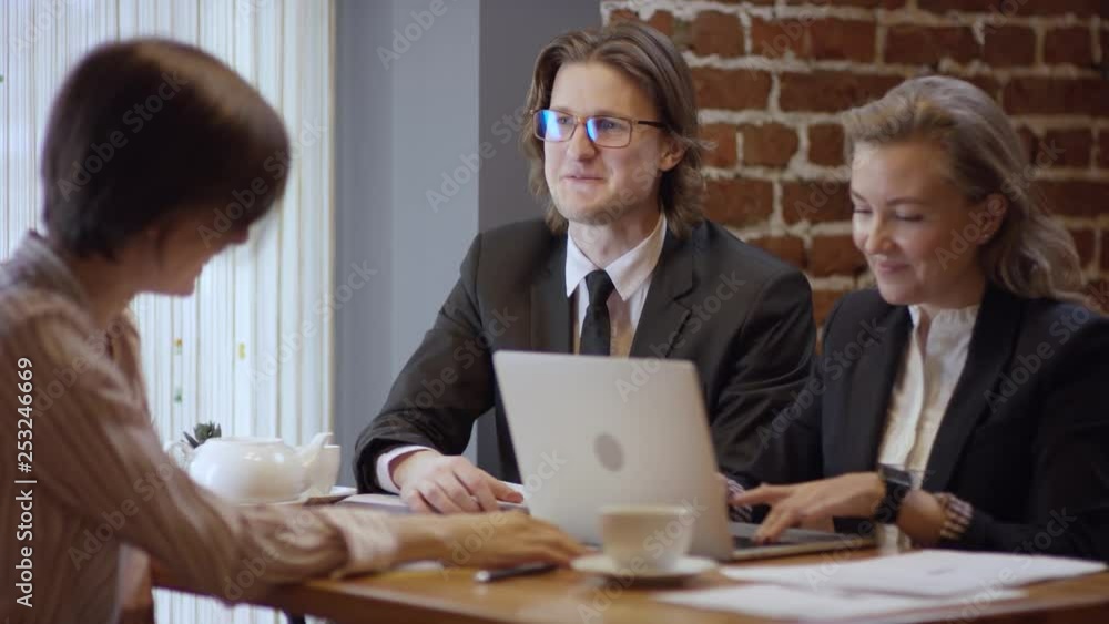 Three people are working together and discussing a contract in a cafe. The women and the man in a restaurant or a coffee shop are drinking coffee. It is a business meeting. They're working on business Three people are working together and discussing a contract in a cafe. The women and the man in a restaurant or a coffee shop are drinking coffee. It is a business meeting. They're working on business