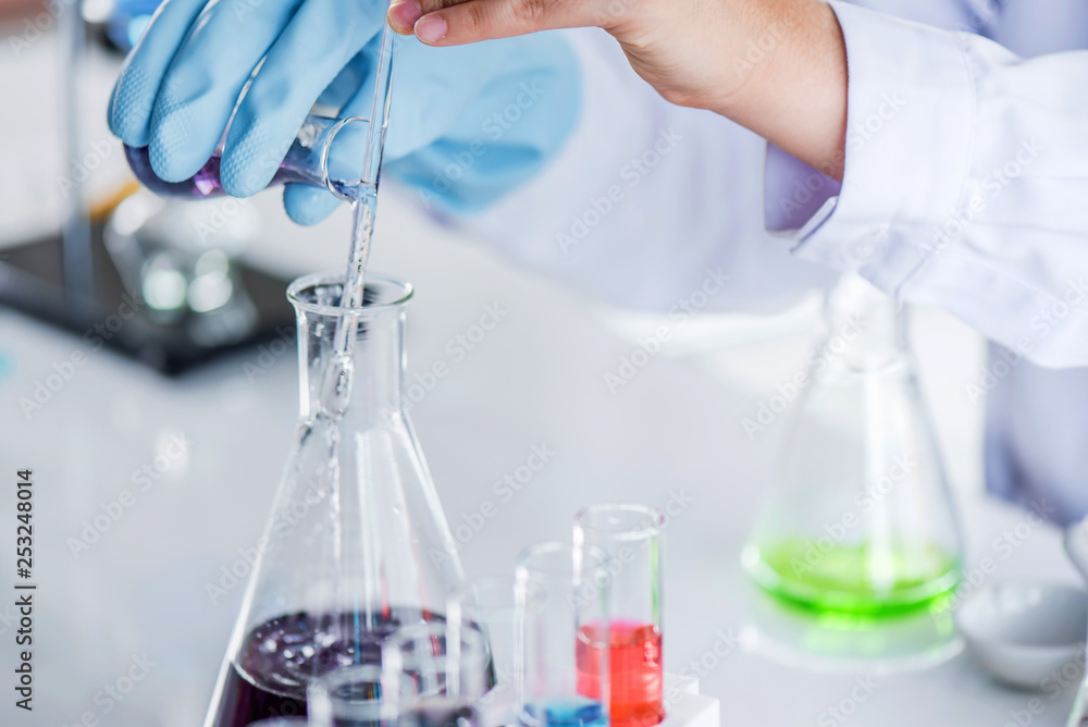 Scientist holding sampling oil or chemical liquid in flask with lab glassware in laboratory background, science or medical research and development concept Scientist holding sampling oil or chemical liquid in flask with lab glassware in laboratory background, science or medical research and development concept