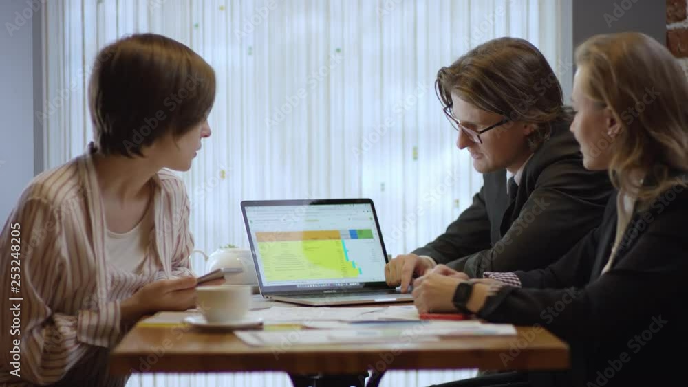 Three people are working together and discussing a contract in a cafe. The women and the man in a restaurant or a coffee shop are drinking coffee. It is a business meeting. They're working on business Three people are working together and discussing a contract in a cafe. The women and the man in a restaurant or a coffee shop are drinking coffee. It is a business meeting. They're working on business