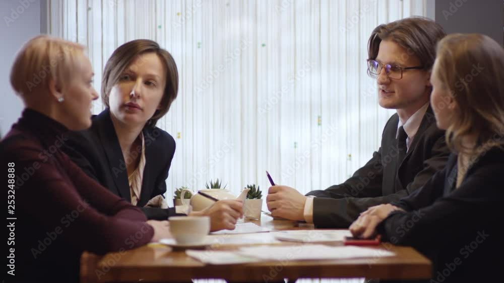 Four people are working together and discussing a contract in a cafe. Three women and the man in a restaurant or a coffee shop are drinking coffee. It is a business meeting. They're working on