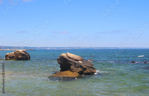 Beautiful sea shore in Sunny summer weather, waves are beating against big rocks sticking out of the water.