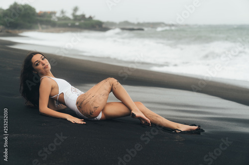 Beautiful sexy girl with long hair lying on beach with black sand. Young woman enjoys relaxing near ocean © romannoru