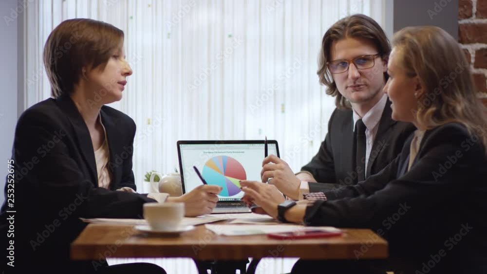 Three people are working together and discussing a contract in a cafe. The women and the man in a restaurant or a coffee shop are drinking coffee. It is a business meeting. They're working on business Three people are working together and discussing a contract in a cafe. The women and the man in a restaurant or a coffee shop are drinking coffee. It is a business meeting. They're working on business