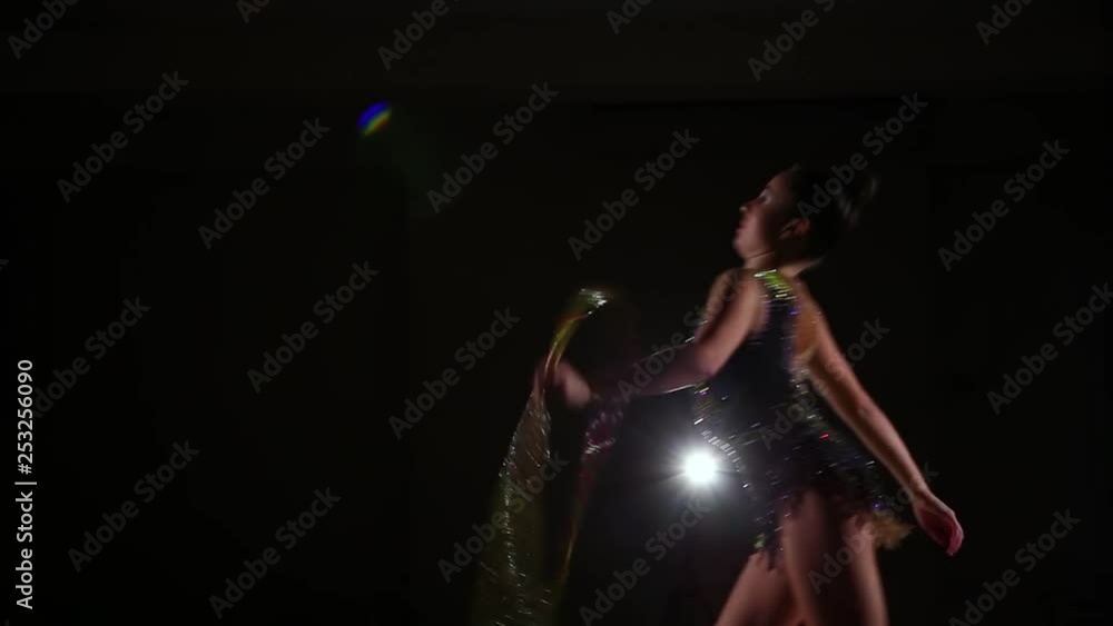 Slim cute attractive girl athlete in bright colorful swimsuit performs elements of rhythmic gymnastics with hoop in dark gym with beautiful staged light and rear light Slim cute attractive girl athlete in bright colorful swimsuit performs elements of rhythmic gymnastics with hoop in dark gym with beautiful staged light and rear light