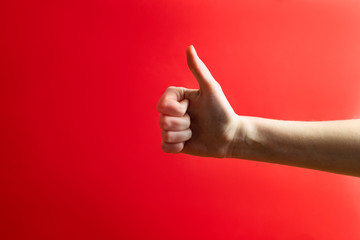 Thumbs up, approval gesture concept. Hand showing a "thumb up" sign in vibrant red background