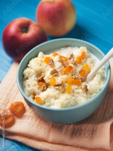 Millet milk porridge with Apple, walnut and dried apricots on a wooden blue background